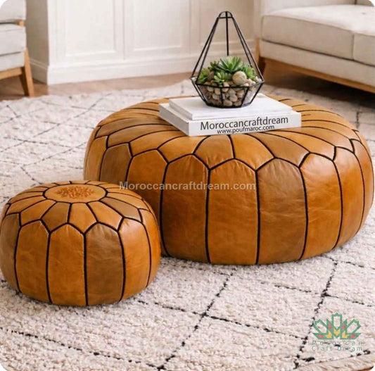 Two tan leather poufs with black stitching on a textured rug with a small plant and book on top, branded 'Moroccancraftdream'.