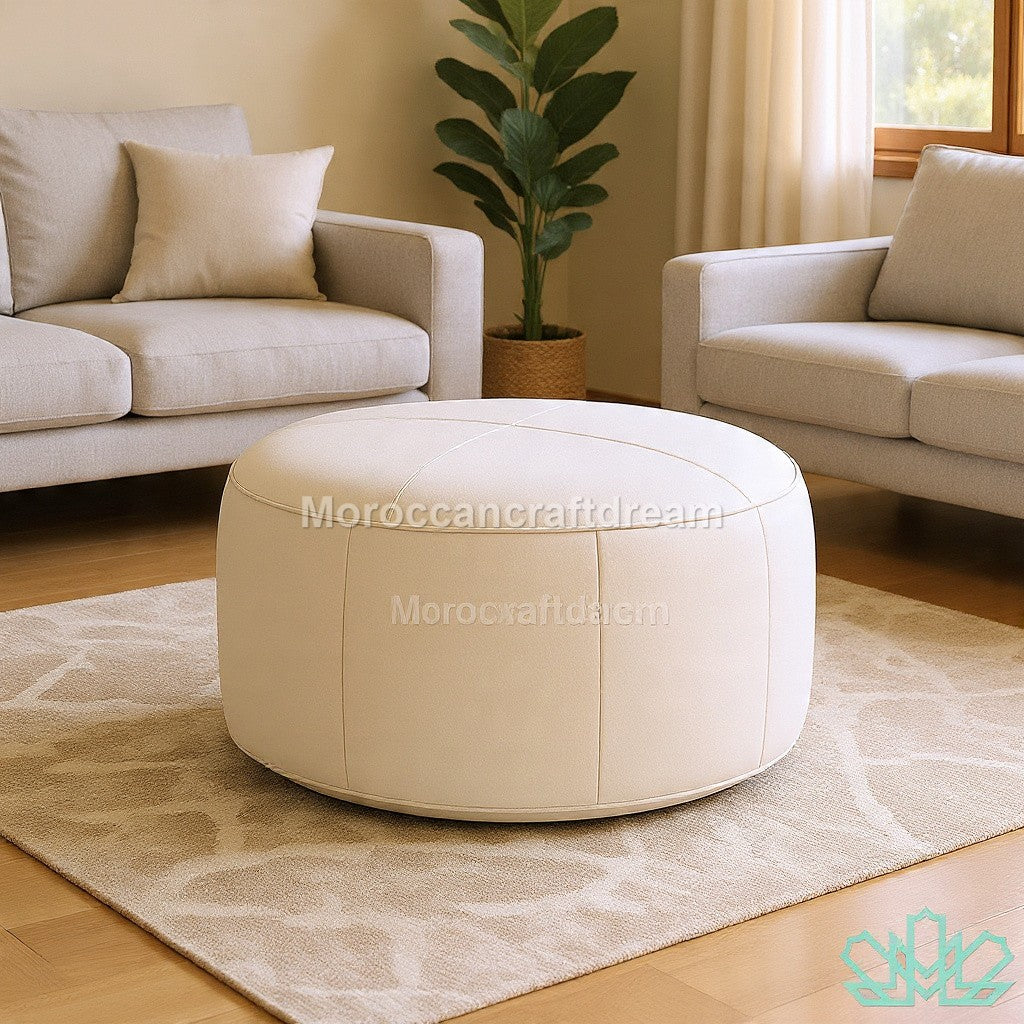Round beige ottoman in a living room setting with beige sofas and a plant.