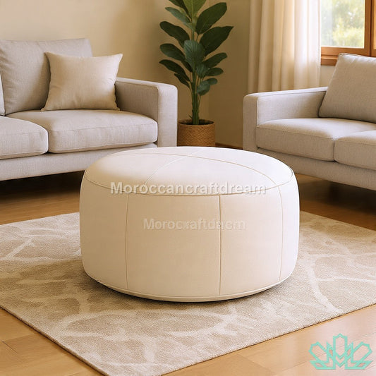 Round beige ottoman in a living room setting with beige sofas and a plant.