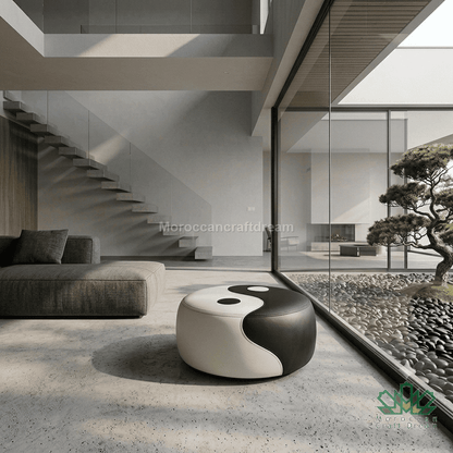 A modern round pouf ottoman with a black and white yin-yang design, placed in a minimalist contemporary living room with a glass wall overlooking a zen garden.